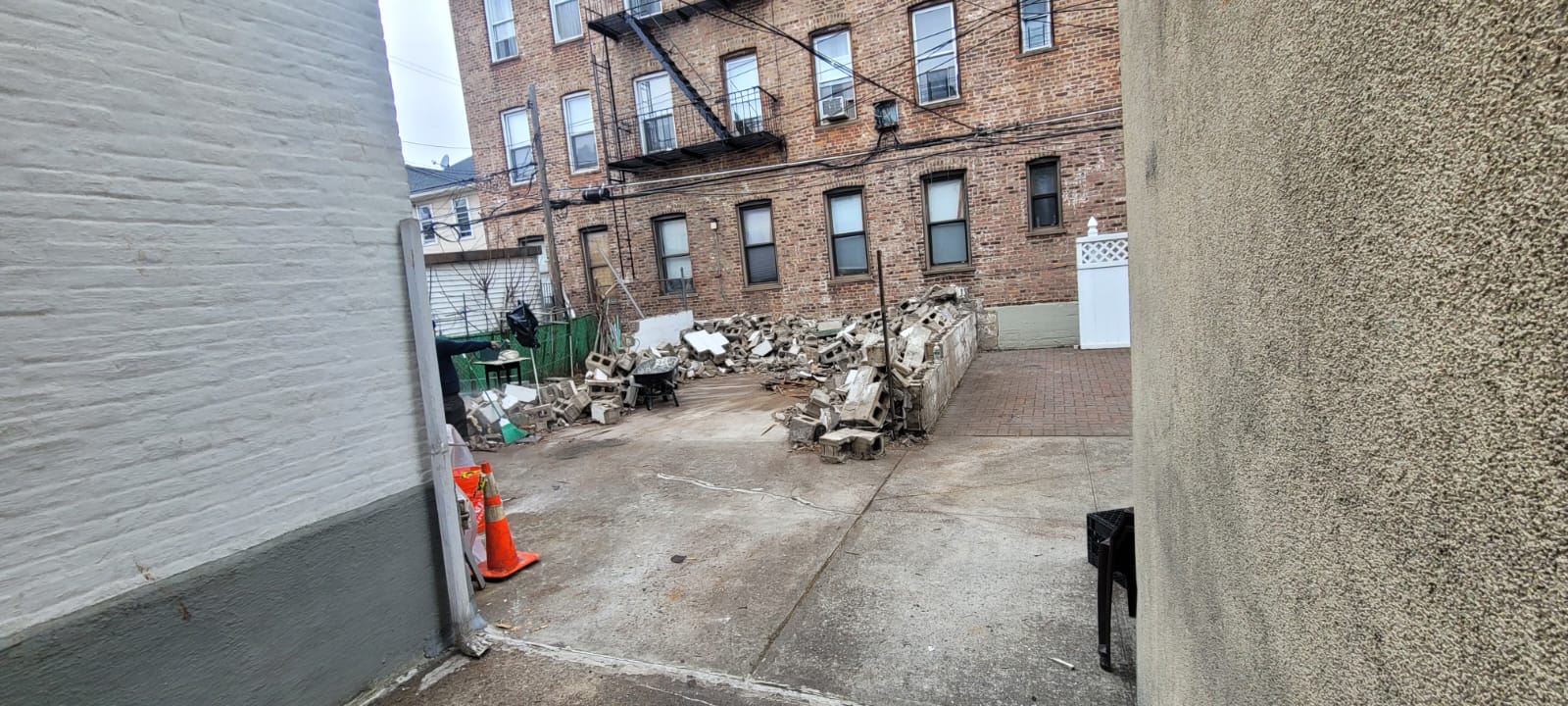 Brooklyn backyard before construction with broken concrete and rubble piled between brick buildings