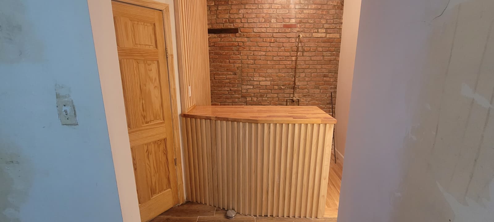 Wide view of the finished slatted wood counter beside restored exposed brick