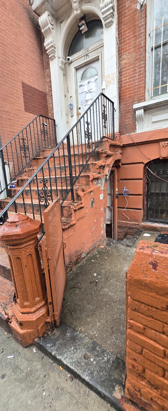 Brooklyn brownstone stoop before restoration with cracked orange painted masonry, damaged pillar and exposed brick